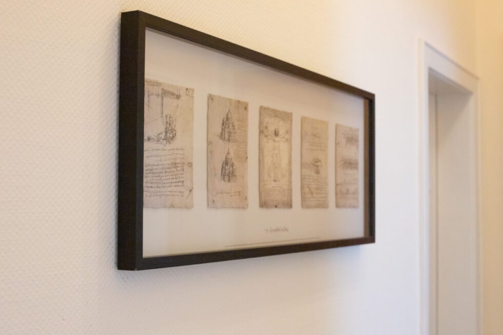 Fünf Bilder von Leonardo da Vinci hängen in einem schwarzen Rahmen an einer Wand.