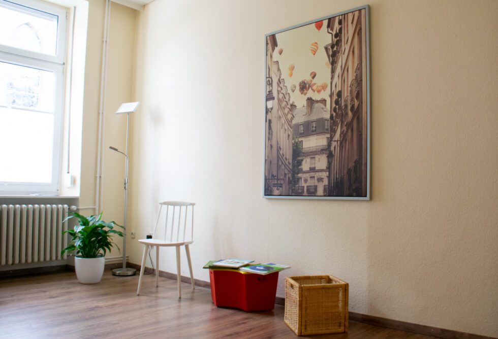 Das Wartezimmer der Logopädie Praxis. Dunkler Laminat, Spielsachen und Sitzmöglichkeiten, an der Wand ein Bild.